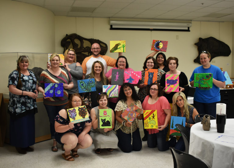 A group of adults holding a various paintings they created